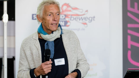 Impulsvortrag von Dipl.-Ing. Dirk Schelhorn, Schelhorn Landschaftsarchitektur Dipl.-Ing. Dirk Schelhorn mit Mikro in der Hand während seines Impulsvortrags, im Hintergrund sind Roll-Ups zu sehen