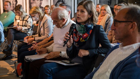 Fragerunde mit den Teilnehmenden Nahaufnahme auf das Publikum während der offenen Fragerunde, hier ist eine Teilnehmerin mit Mikro in der Hand zu sehen, Blick ist Richtung Bühne gedreht.