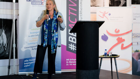 Impulsvortrag von Gundi Friedrich, Landessportbund Hessen e. V. Gundi Friedrich (Landessportbund Hessen e.V.) steht links vom Rednerpult mit Mikro in der Hand während Ihres Impulsvortrages.