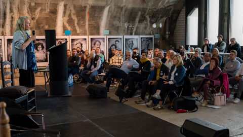 Impulsvortrag von Gundi Friedrich, Landessportbund Hessen e. V. Seitenansicht: rechts ist der voll besetzte Teilnehmendenkreis zu sehen, links davon Gundi Friedrich auf der Bühne während Ihres Impulsvortrages
