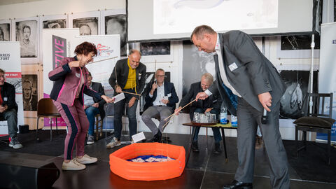 Intersektoral besetzte Diskussionsrunde rund um Anliegen der Bevölkerung und der Teilnehmenden Einzelne Podiumsgäste sind aufgestanden um mit einer Angel Fragen der Bevölkerung aus einem in der Mitte liegenden Planschbecken zu fischen.