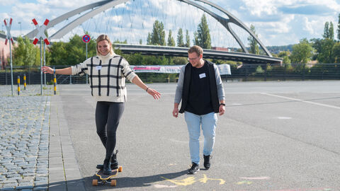Vielfältiges Bewegungsprogramm auf dem Hafenparkgelände zum Mitmachen: Sportmobil Adventure Cube (Sportjugend Hessen) Vielfältiges Bewegungsprogramm auf dem Hafenparkgelände zum Mitmachen: Sportmobil Adventure Cube (Sportjugend Hessen). Hier probiert links eine Teilnehmerin das Skateboarden aus, rechts von ihr steht ein Vertreter der Sportjugend Hessen.