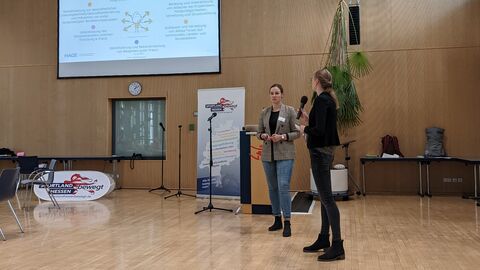 Vorstellung der Good Practice-Kriterien durch die KGC Hessen, vertreten durch Anna Kleine und Claudia Ostermann (vorne rechts im Bild). Links oben im Bild ist die Leinwand mit Präsentation zu sehen.