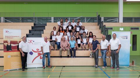 Gruppenbild der Absolvent*innen der C-Lizenz-Ausbildung mit ihren Zertifikaten, sowie Ausbilder*innen und weitere Beteiligte. Das Bild wurde in einer Sporthalle aufgenommen, rechts und links sind die Organisatoren zu sehen, mittig die Teilnehmenden.