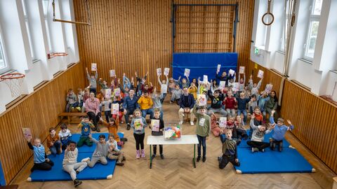 Foto aus Vogelperspektive der Preisverleihung in einer Sporthalle. Viele Kinder inkl. die Organisatoren halten ihre Urkunde in die Luft.