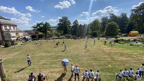 Rasenfläche mit zweit Toren aus Vogelperspektive. Es wird Fußball gespielt. Menschen schauen vom Rand zu.