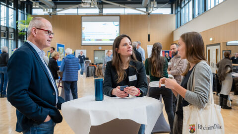 Teilnehmende beim Netzwerken vor Beginn der Veranstaltung Menschen an Stehtisch unterhalten sich