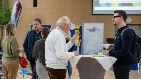 Teilnehmende beim Netzwerken vor Beginn der Veranstaltung Menschen an Stehtisch unterhalten sich