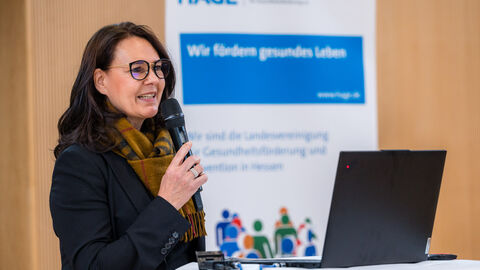 Offizielle Begrüßung der Teilnehmenden durch die Geschäftsstelle des Landesprogramms SPORTLAND HESSEN bewegt (Petra Kraus, HMFG) Frau mit Mikrofon an Rednerpult