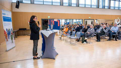 Zuhörerinnen und Zuhörer lauschen gespannt der offiziellen Begrüßung durch die Geschäftsstelle des Landesprogramms SPORTLAND HESSEN bewegt (Petra Kraus, HMFG) Frau an Rednerpult, Plenum hat die Aufmerksamkeit auf Sie gerichtet