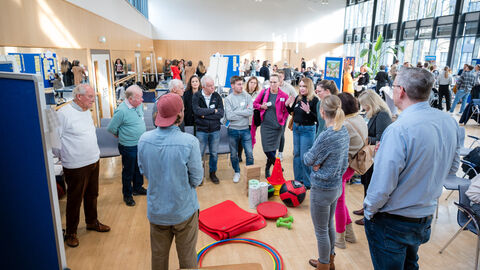 Teilnehmende im Austausch im Rahmen der Diskussionsrunde Eine Gruppe von Menschen stehen um eine Pinnwand und sprechen miteinander