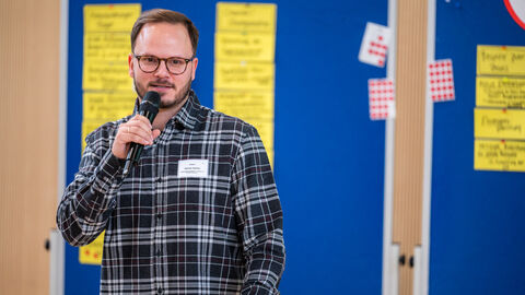 Dominic Günther (Bewegungskoordinator des Vogelsbergkreises) bei der Vorstellung eines Beispiels guter Praxis Mann mit Mikrofon in der Hand vor Pinnwand