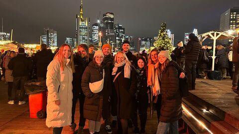 Ein Gruppenbild auf dem Weihnachtsmarkt vor dem Hintergrund der beleuchteten Frankfurter Skyline.