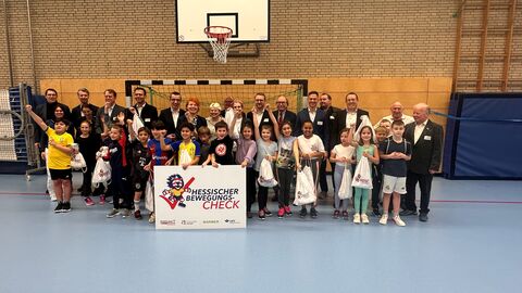 Gruppenbild mit Schüler und Schülerinnen und Gästen der Auftaktveranstaltung in der Sporthalle unter Basketballkorb