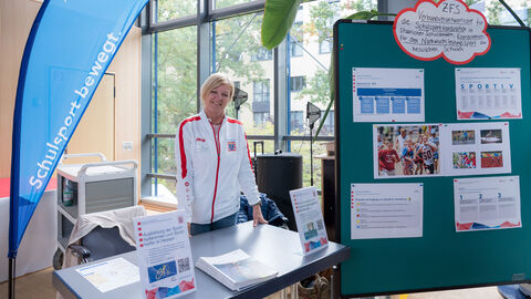 Eine Ausstellerin steht an ihrem Stand, hinter ihr ist ein Roll-Up und eine Pinnwand zu sehen.