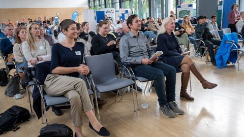 Teilnehmende sitzen bei der Eröffnung der Veranstaltung auf ihren Stühlen