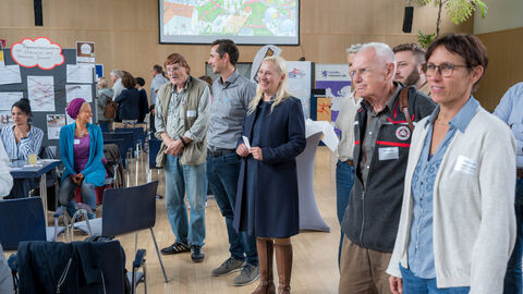Gruppe von Personen lauschen einem Vortrag an einer Pinnwand