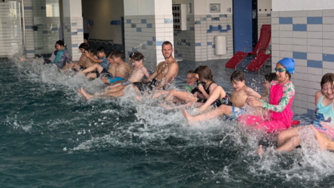 Kinder strampeln am Beckenrand mit ihren Beinen Übung zur Wassergewöhnung – spielerisches Kennenlernen von Wasserwiderstand und Strömungen