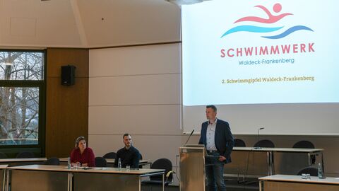Austausch beim zweiten Schwimmgipfel Waldeck-Frankenberg  Mann am Rednerpult in Konferenzsaal mit einer Präsentation im Hintergrund
