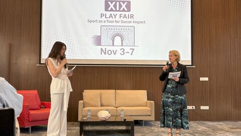 Zwei Frauen stehen auf der Bühne neben einer Couch. Ene Präsentation ist im Hintergrund zu sehen