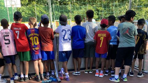 Viele Kinder stehen um enen SPortplatz und schauen dem Geschehen zu. 