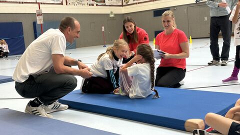 Drei Erwachsene feuern Kinder bei Sportübung in der Sporthale an